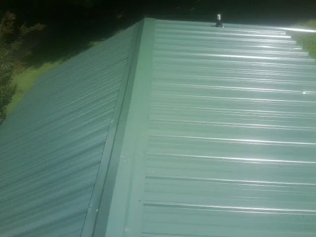 New green metal panels meeting at the ridge of a roof — Flat Roof Repair work by our crew in Marysville